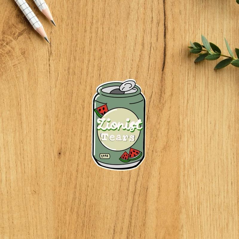 Sticker of a can labeled 'zionist Tears' on a wooden surface with pencils and leaves.