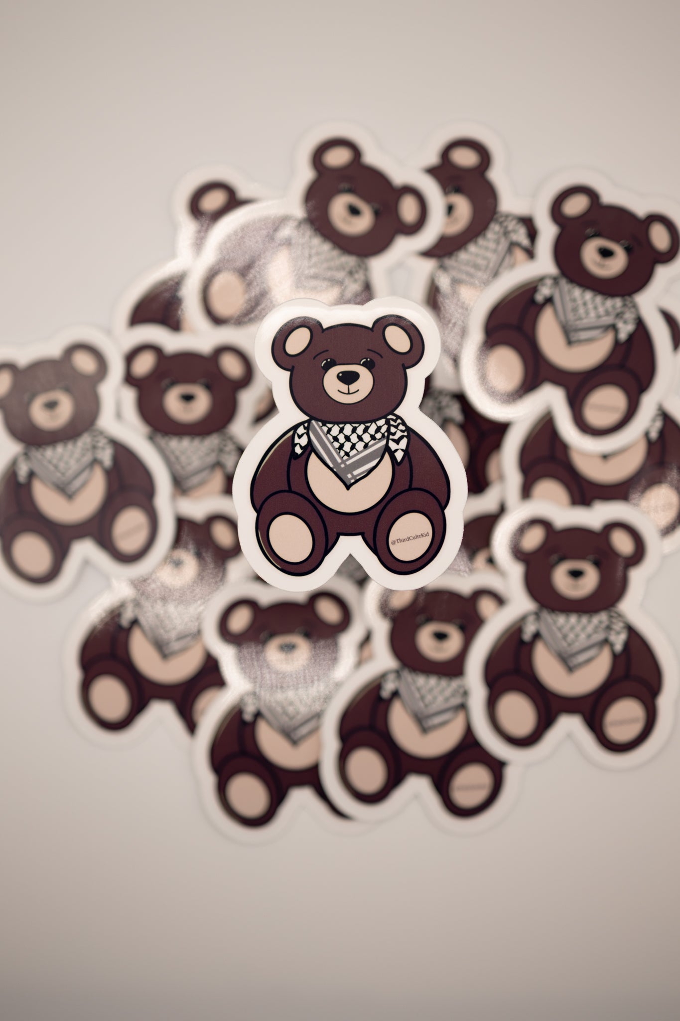 Sticker of a teddy bear with a checkered scarf surrounded by similar teddy bear stickers on a plain background.