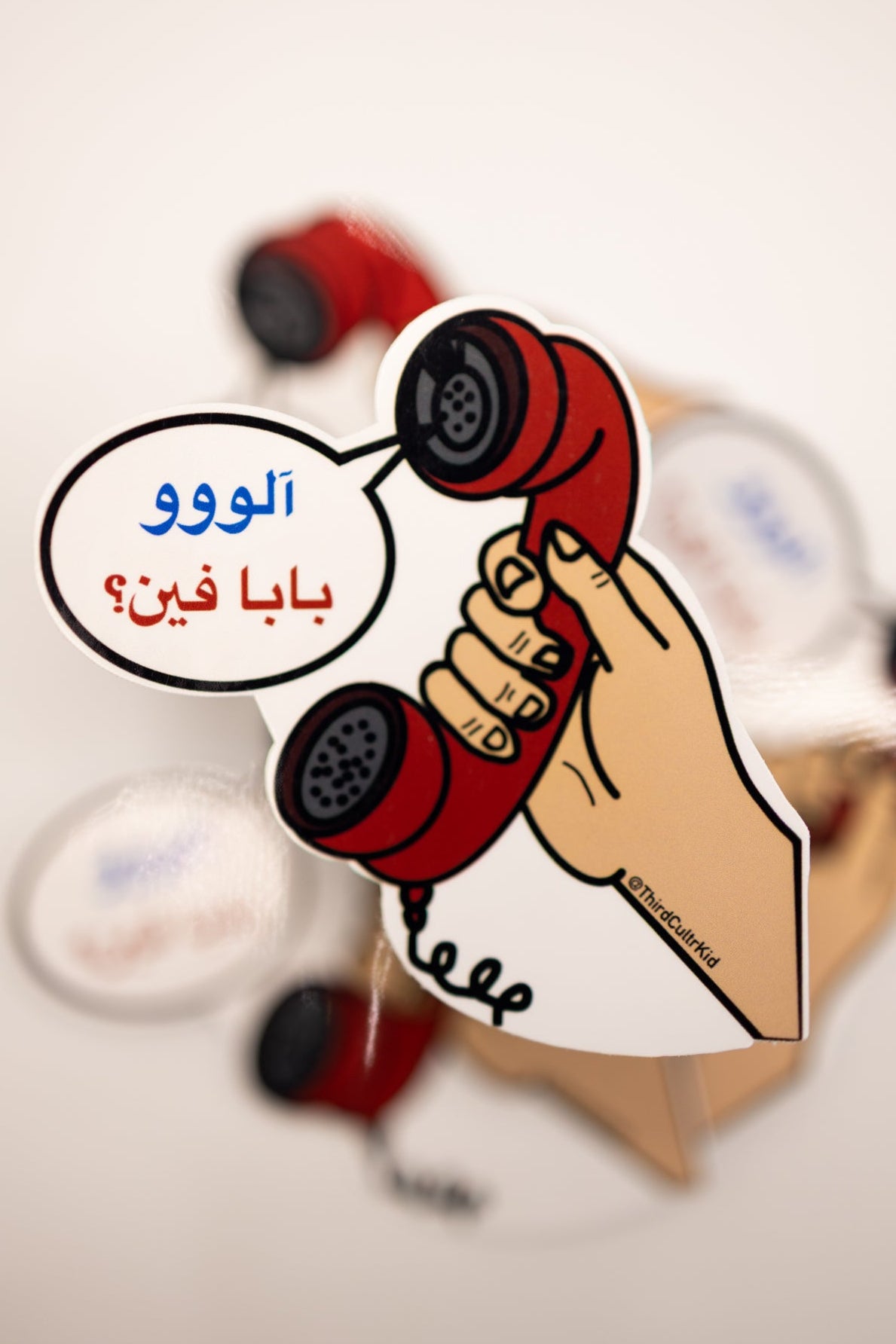 Cartoon hand holding a red phone with Arabic text on a white background