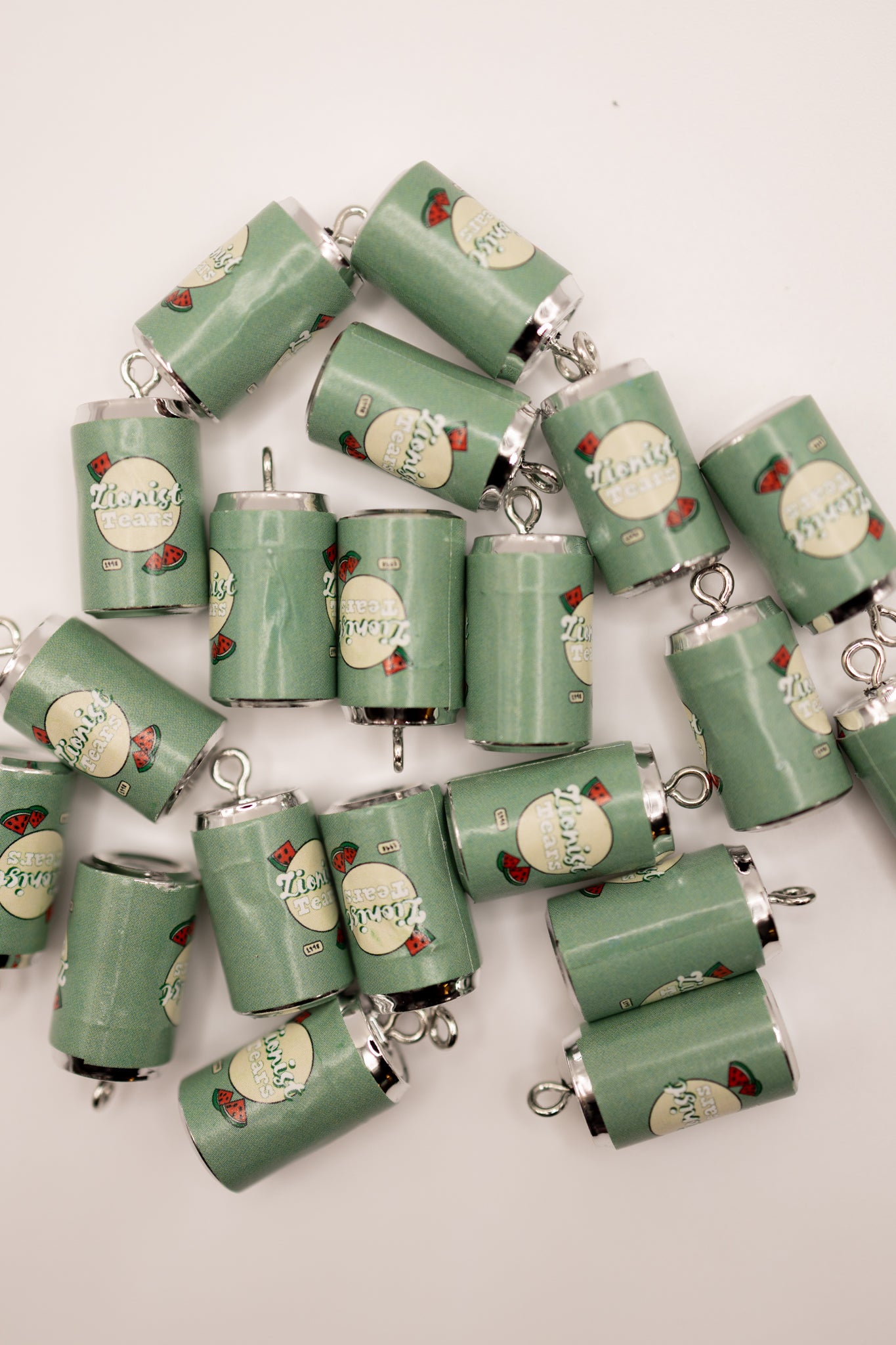 Collection of green cylindrical charms with 'zionist tears' text and decorative elements on a white background
