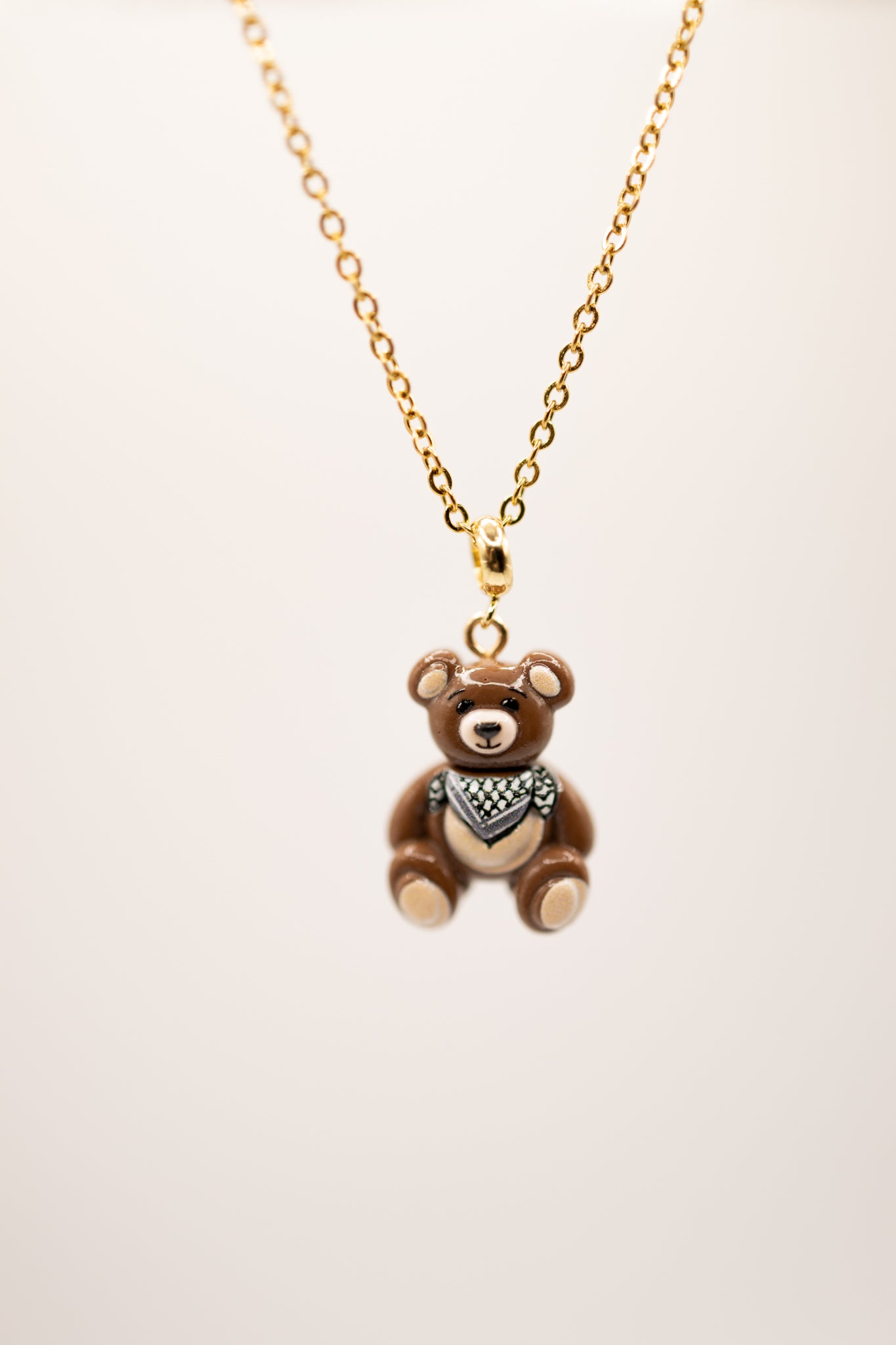Gold necklace with a teddy bear pendant on a beige background