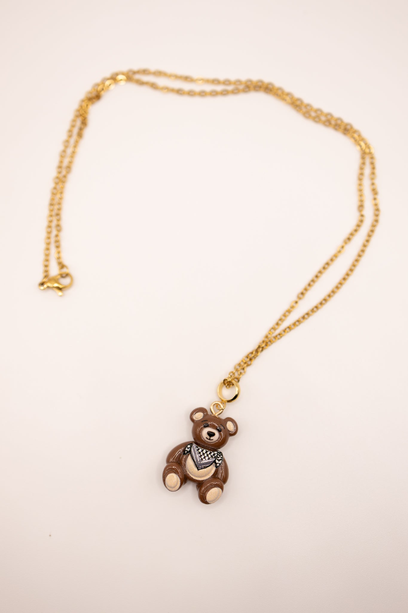 Gold necklace with a teddy bear pendant on a beige background
