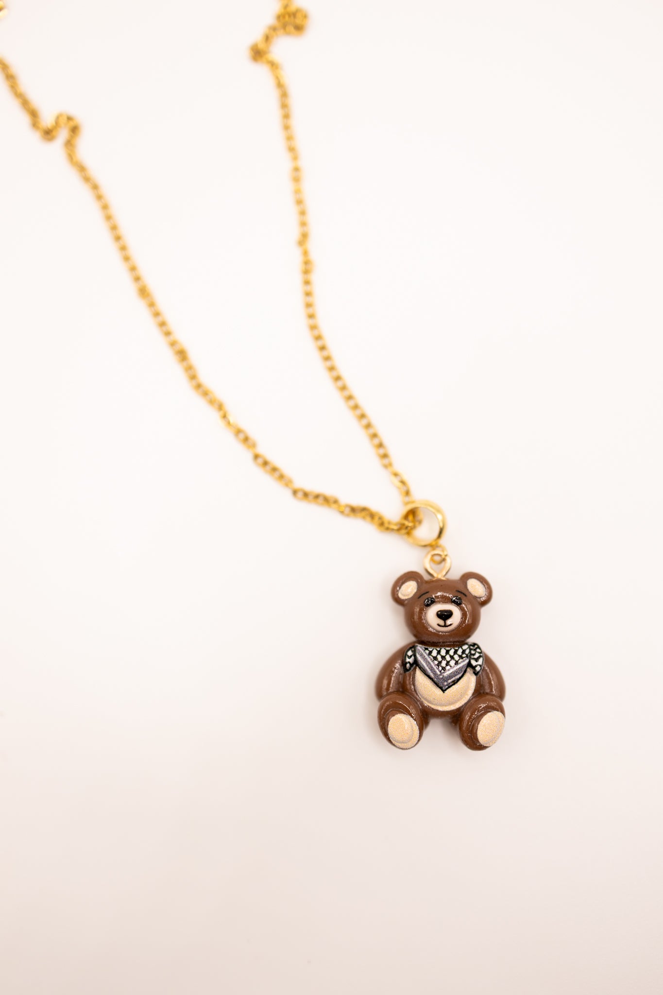 Gold necklace with a teddy bear pendant on a beige background