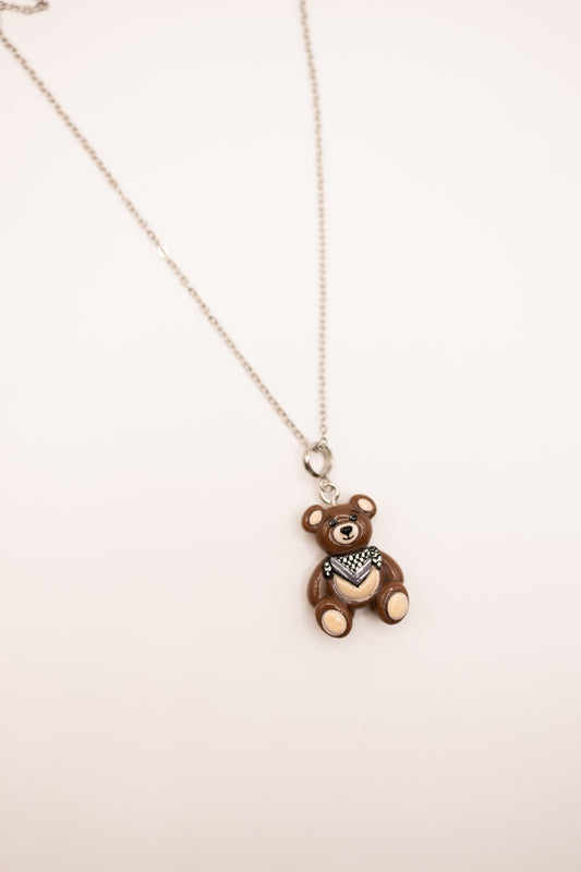 Brown teddy bear pendant on a silver chain against a light background