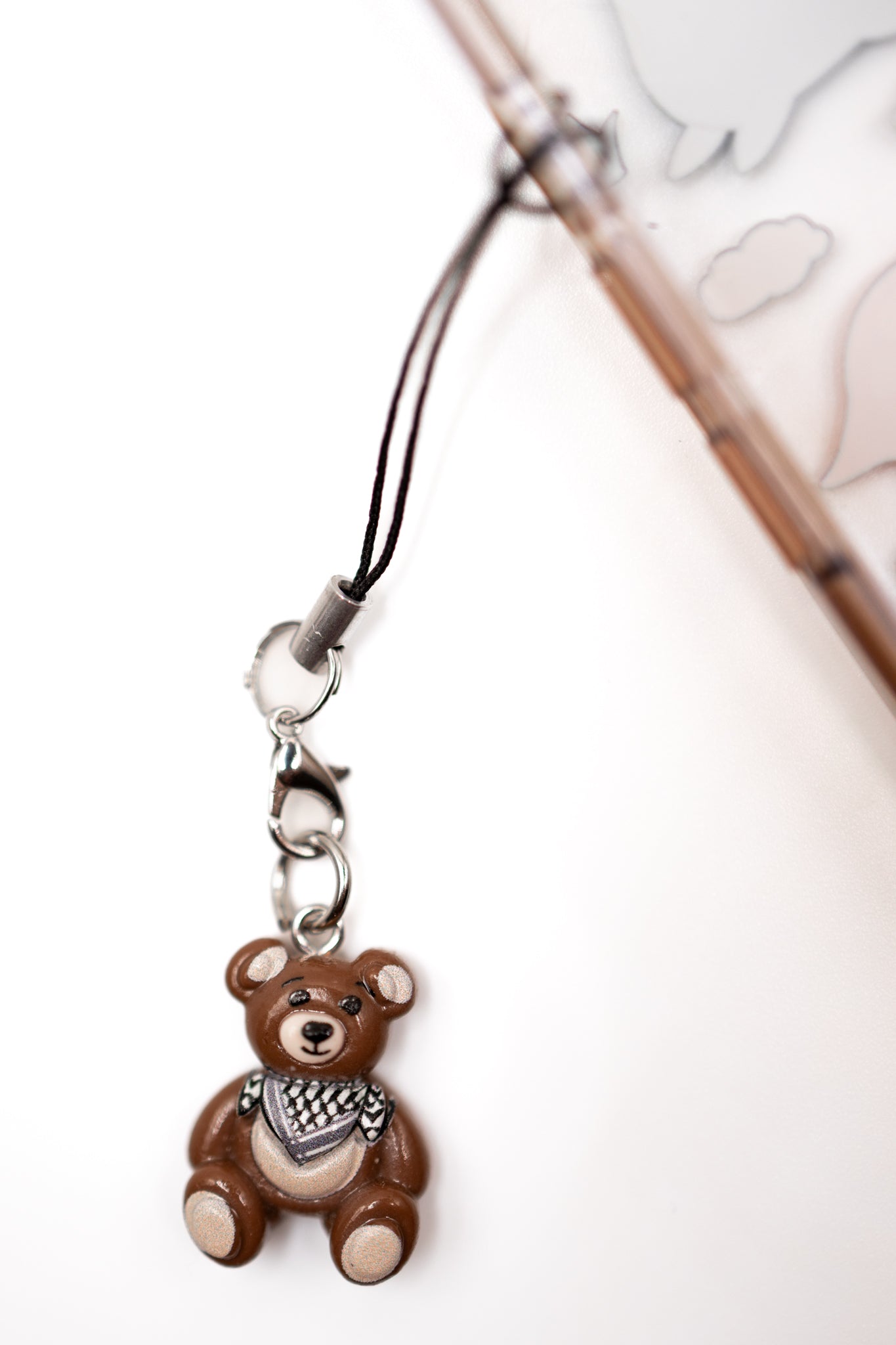 Brown keffiyeh teddy bear phone charm with a black strap on a white background