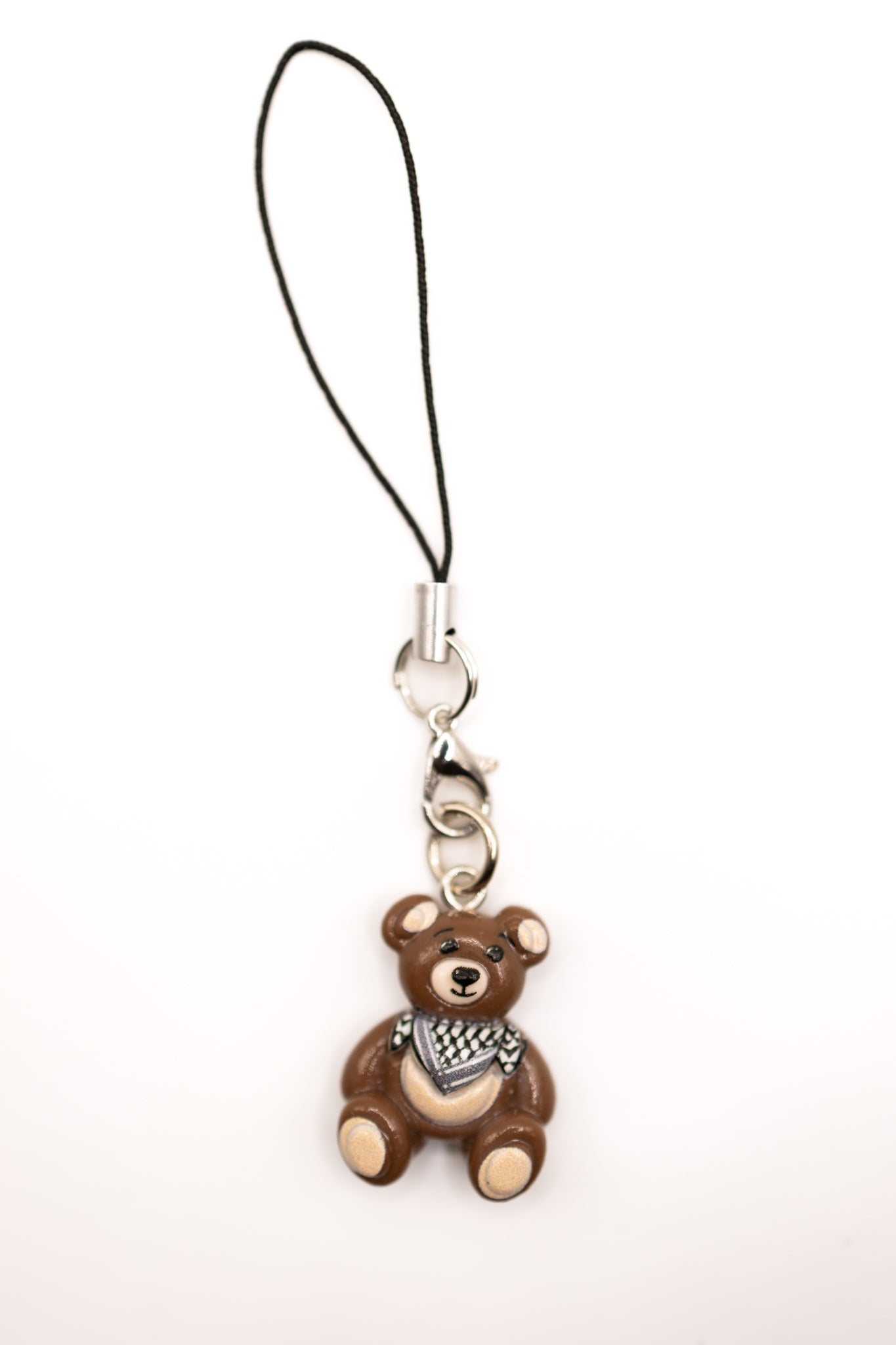 Brown keffiyeh teddy bear phone charm with a black strap on a white background