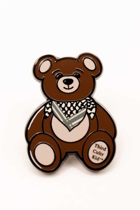 Brown teddy bear pin with a keffiyeh and 'Third Cultur Kid' text on a white background
