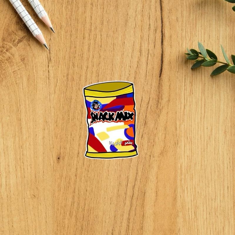 Colorful 'Snack Mix' bag sticker on a wooden surface with pencils and a plant leaf.