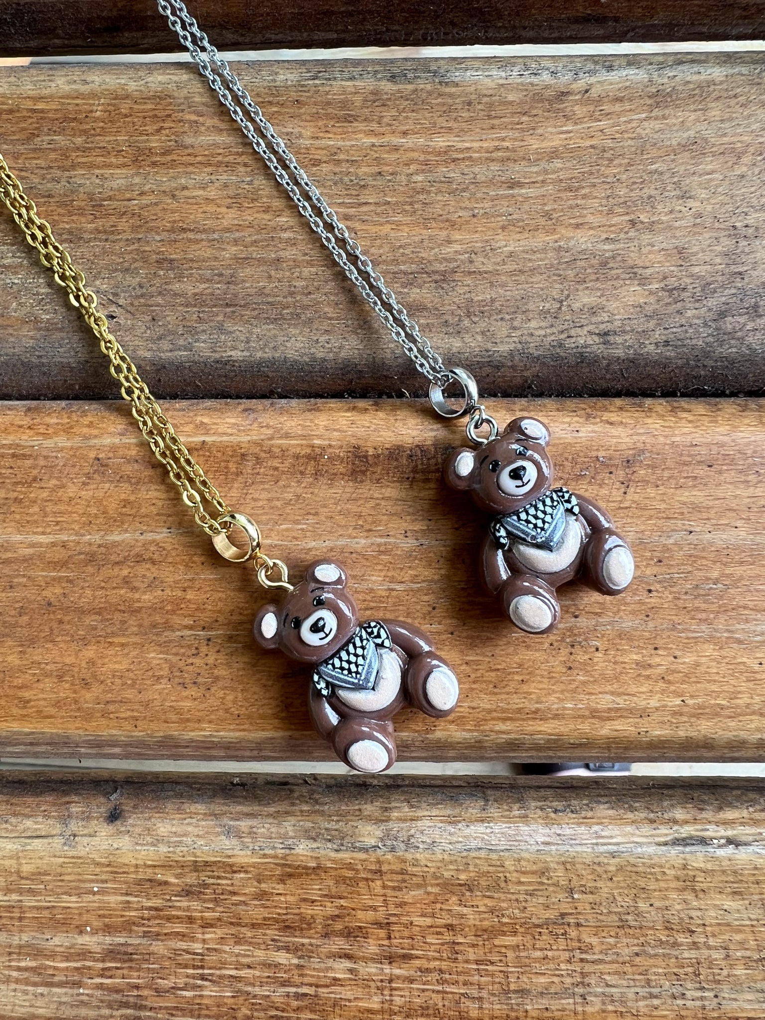 Two teddy bear-shaped pendants on gold and silver chains on a wooden surface.