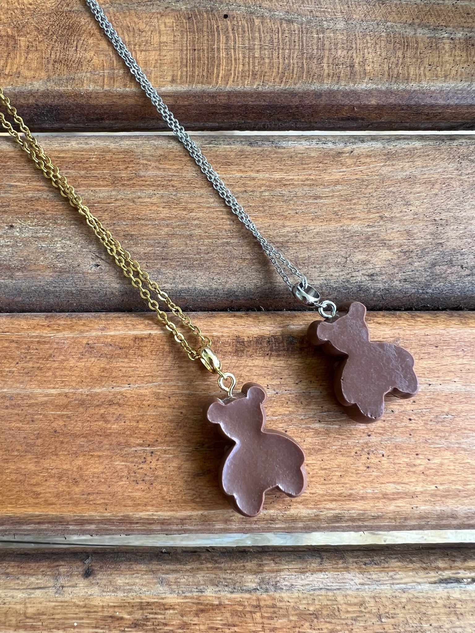 Two brown bunny-shaped pendants on gold and silver chains against a wooden background