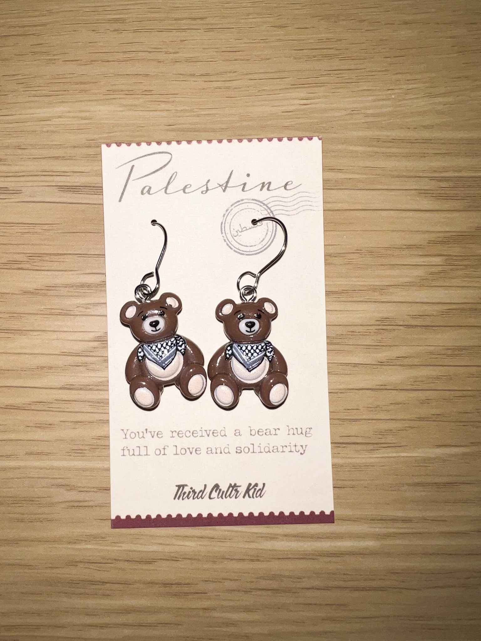 Card with teddy bear earrings and text on a wooden surface