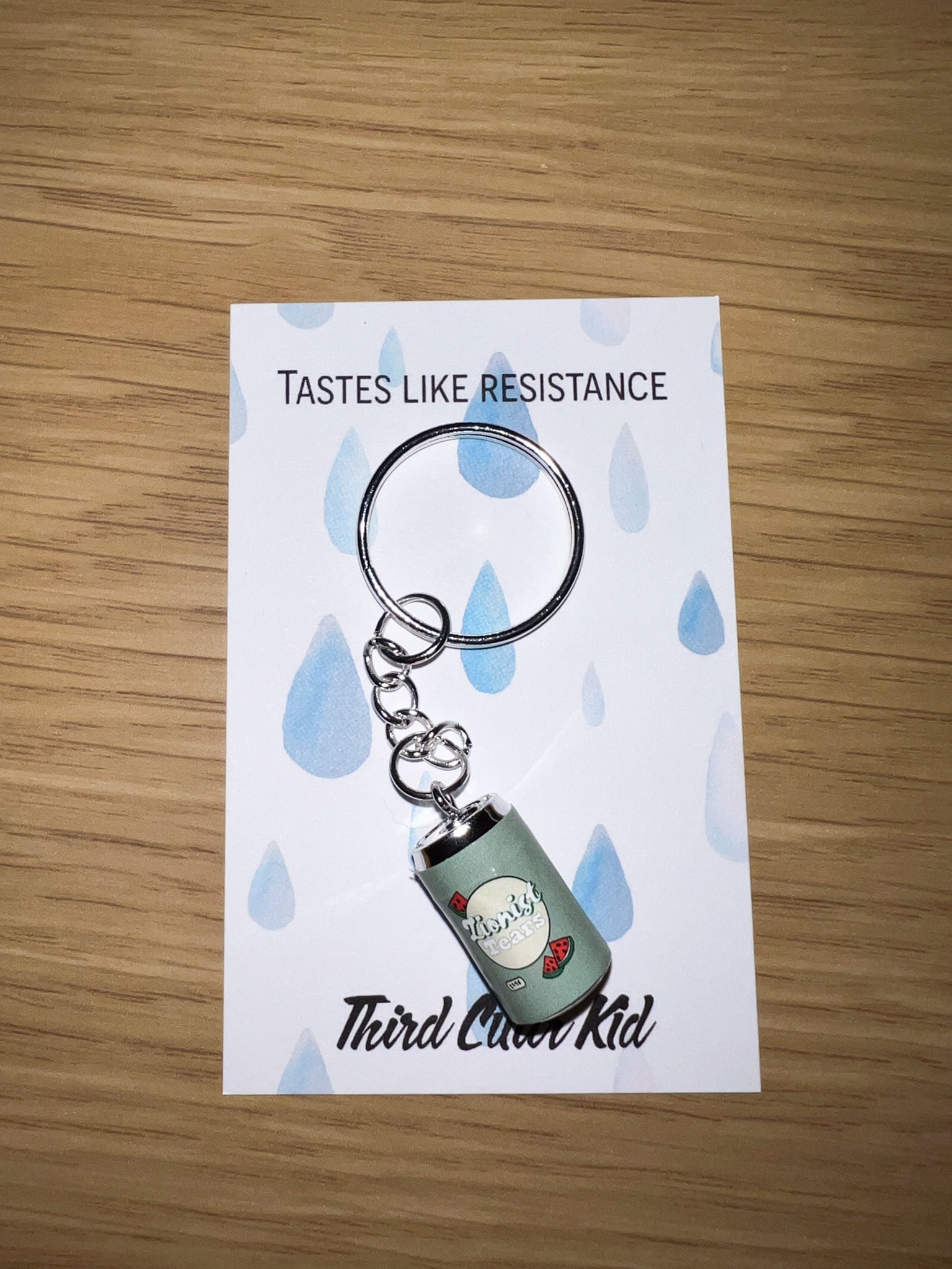 Keychain with 'Tastes Like Resistance' text on a card with blue raindrop design