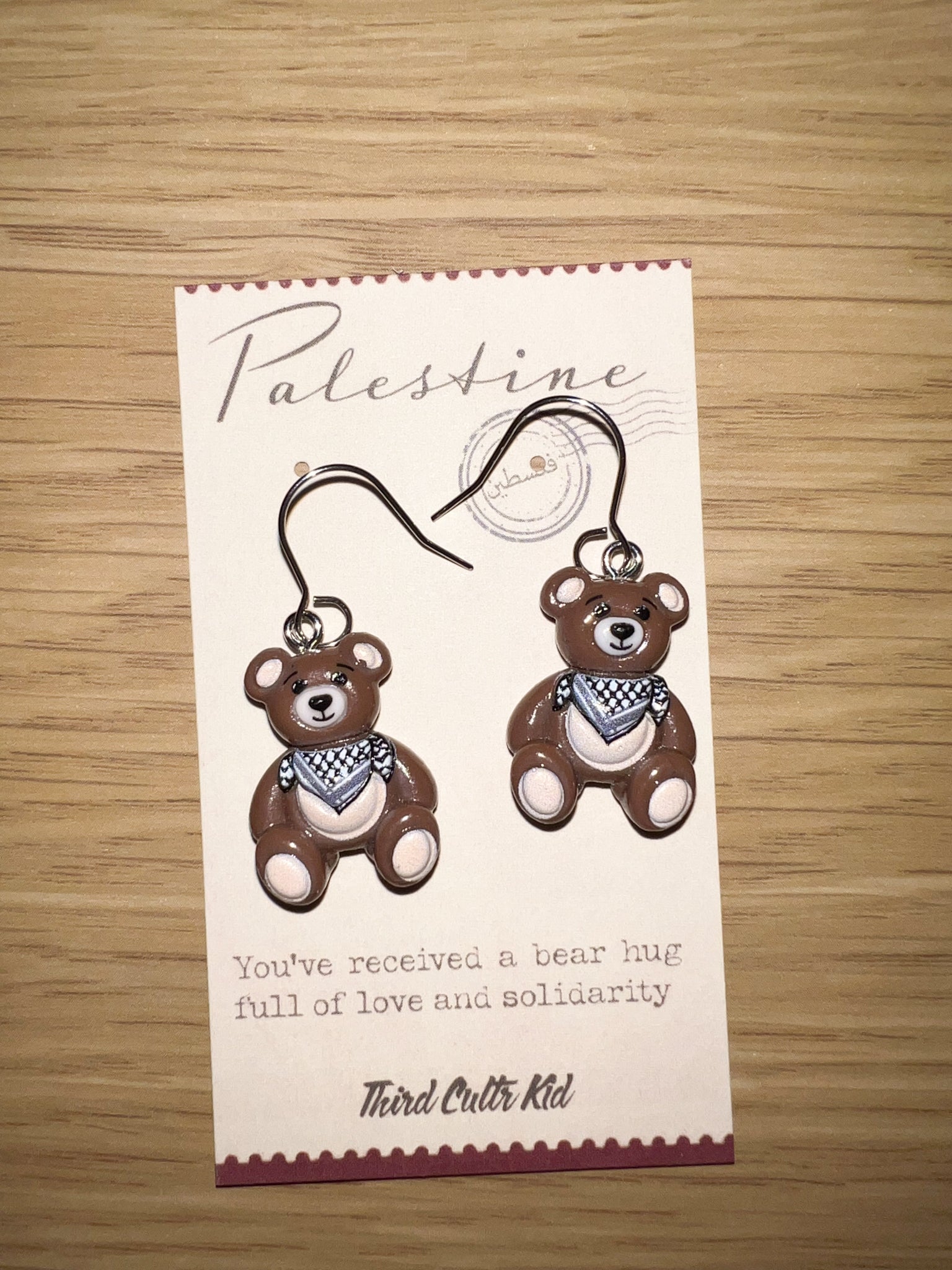 Card with teddy bear earrings and a message on a wooden surface
