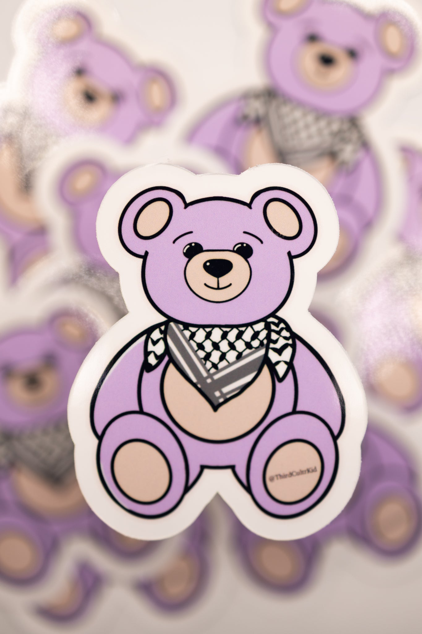 Purple teddy bear sticker with a keffiyeh scarf on a lilac background