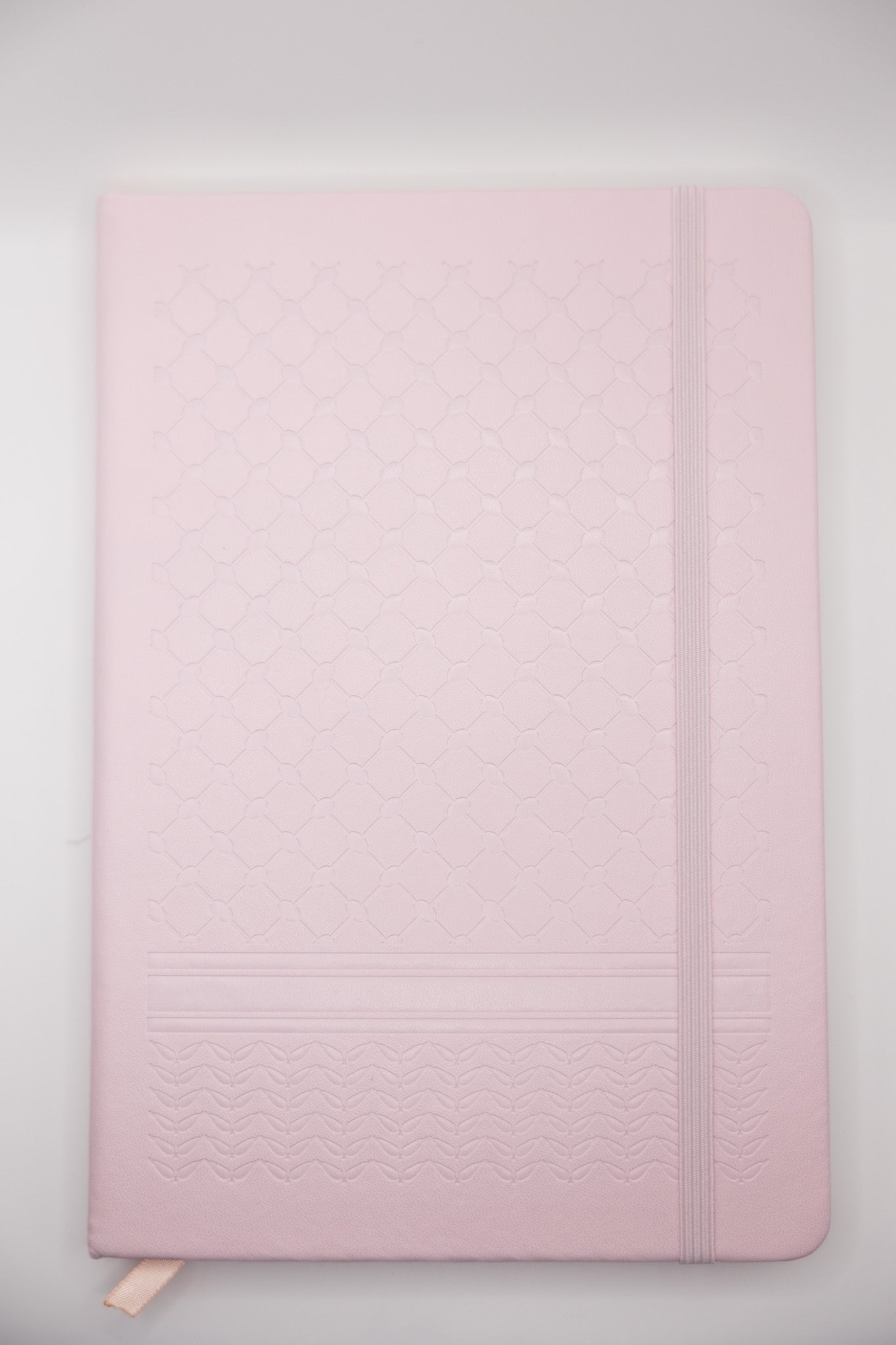 Pink notebook with a keffiyeh textured cover on a light gray background