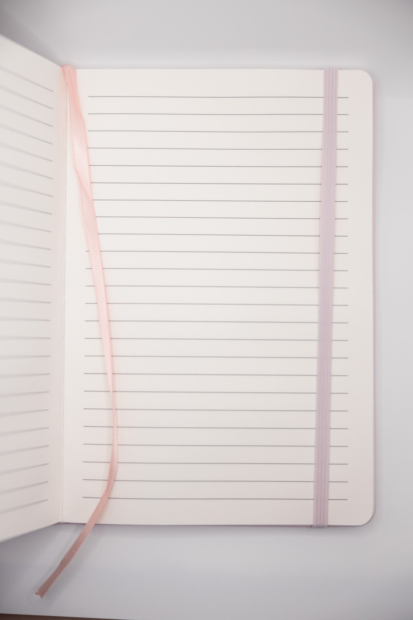 Open notebook with lined pages and a pink ribbon on a light gray background
