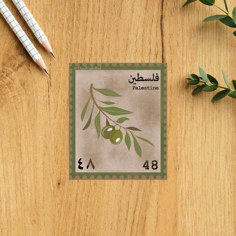 Postcard with olive branch design and 'Palestine' text on a wooden surface with pencils and leaves.