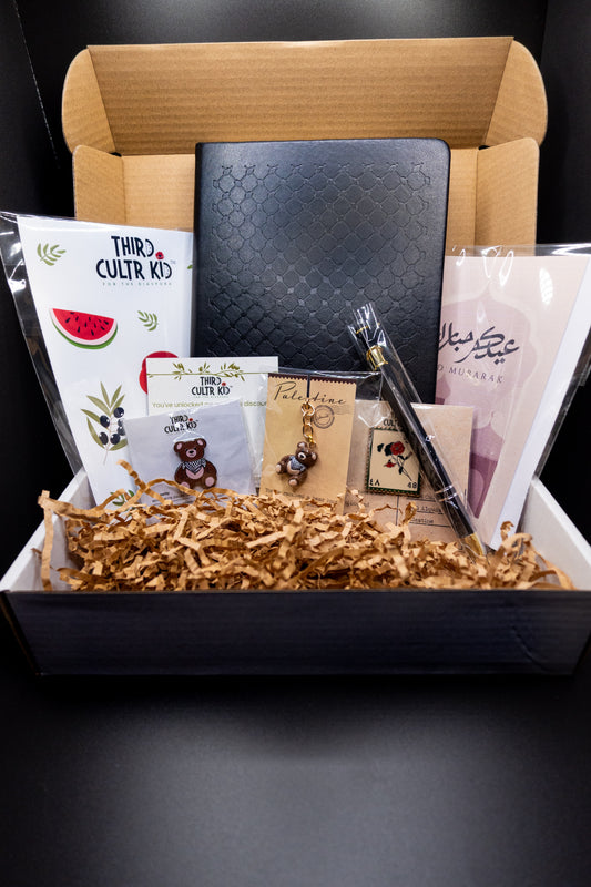 Eid and Ramadan gift box with stationery items including a keffiyeh notebook, pen, enamel pins, sticker sheet, greeting cards on a dark background