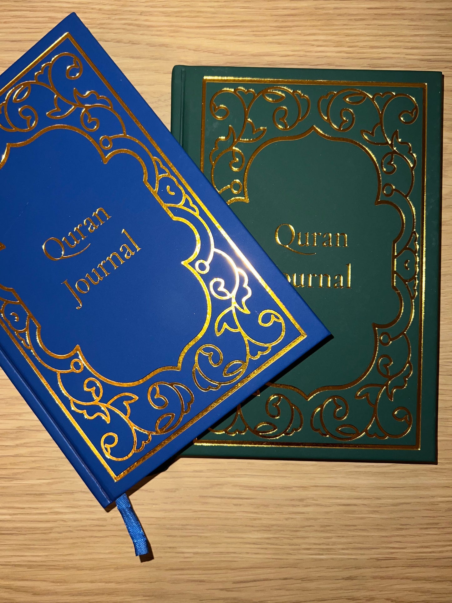 Blue and green Quran journals with ornate designs on a wooden surface